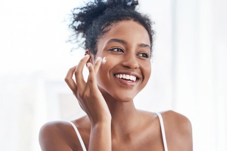Lächelnde Frau demonstriert, wie sie sich eincremt ihrer Wange als Teil ihrer Routine für reine Haut